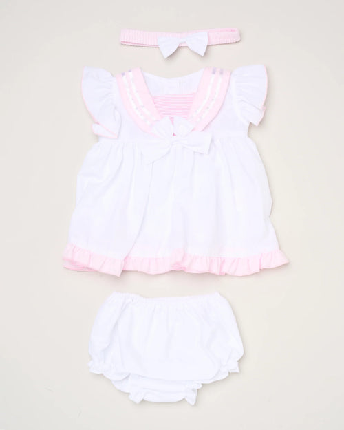 The Baby Girls Dress, Pant & Headband Set features a white dress with pink trim and ruffles, a matching white diaper cover, and a pink headband with a white bow, beautifully displayed on a light background.